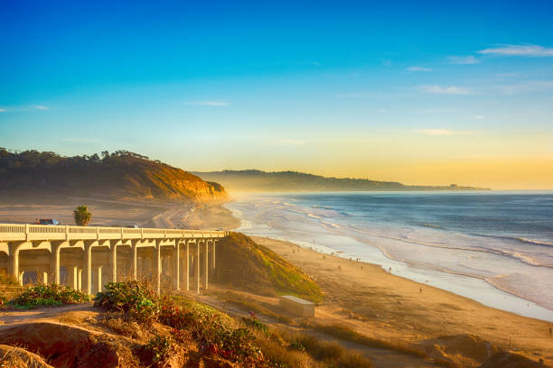 Küstenlandschaft mit einer Bogenbrücke über einem Sandstrand im Abendlicht