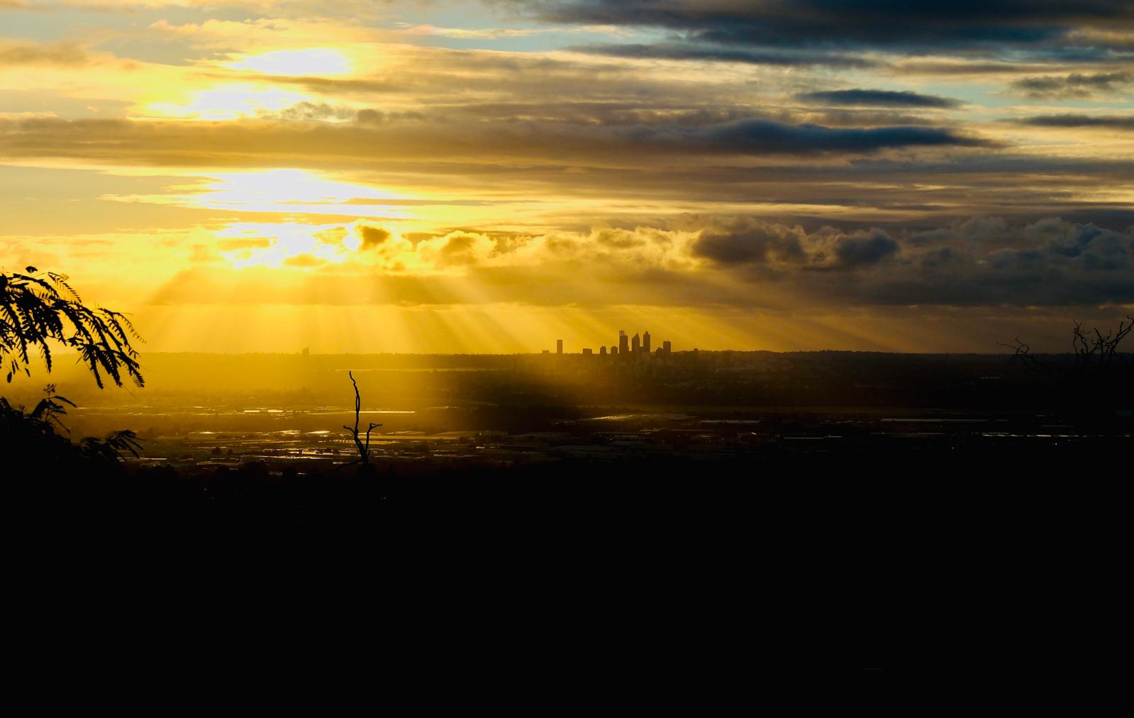 Sonnenstrahlen brechen durch Wolken über einer fernen Skyline im Abendlicht